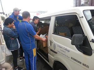 Left: Assistant Headmaster, Middle School, Michael Mullin, wearing cap and Director of Religious Studies Billy Hadnett, back to camera, watch as students load a St Peter’s College van with cans for delivery.