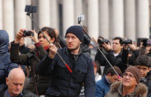 People take photos using selfie sticks while waiting for Pope Francis to appear on the central balcony of St Peter’s Basilica at the Vatican last year. (CNS photo)