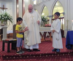 Benedict Thomas plays the violin during the January 9 vigil Mass. Above: Benedict and his brother, Isaac, in altar server garb, present the funds they raised to Msgr Paul Farmer