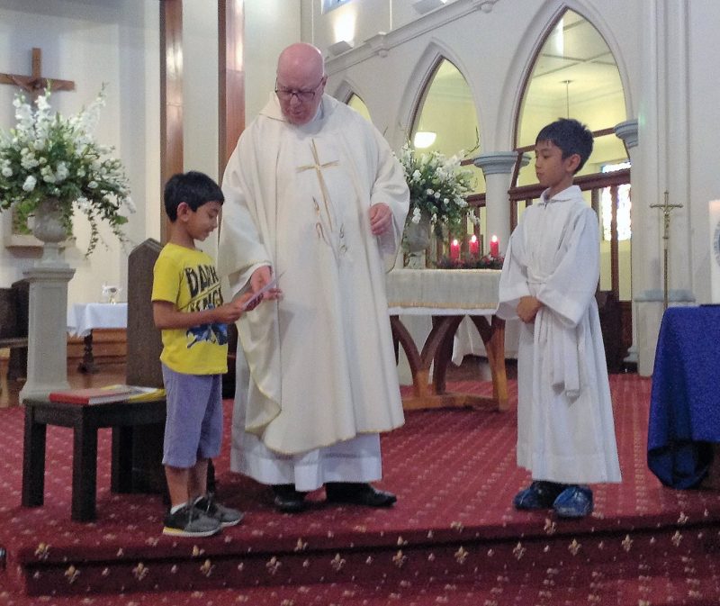 Benedict Thomas plays the violin during the January 9 vigil Mass. Above: Benedict
and his brother, Isaac, in altar server garb, present the funds they raised to
Msgr Paul Farmer