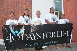 Four young people from the Mother of Divine Mercy Refuge, and an Onehunga parish priest, hold a pro-life banner before the start of Mass at Good Shepherd Church: From left, Sinapi Leaegalesolo, Peata Makaafi, Fr Talepope Varfale, MF, Paul Nuia and Jacinta Uepa.