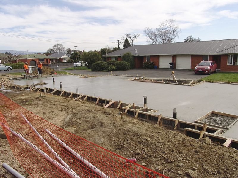 Concrete workers putting the finishing touches on the floor pad for the two house units, with one of the earlier versions in the background.
