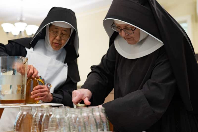All Saints Sister of the Poor Margaret Muraki, left, and All Saints Sister of the Poor Emily Ann Lindsey screw caps onto jars of honey produced by bees on the sister's property in Catonsville, Md., Aug. 16, 2022.  (CNS photo/Kevin J. Parks, Catholic Review)